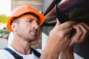 A Man In An Orange Hat And Blue Overalls Installing Gutter Protection For A Home.