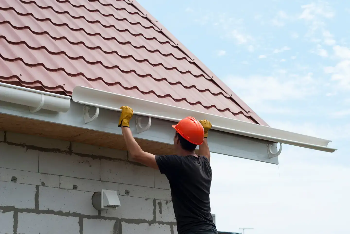 A Man With A Black T-Shirt And A Red Hard Hat Repairing A Gutter.
