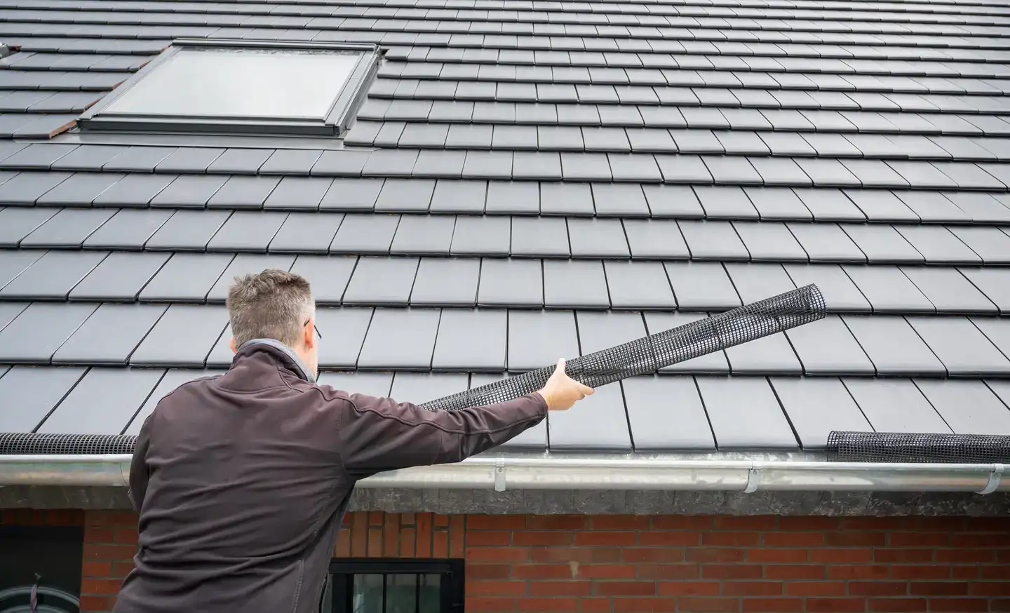A Man In Light Maroon Jacket Installing A Micro Mesh Gutter Guard Protection System On A House.