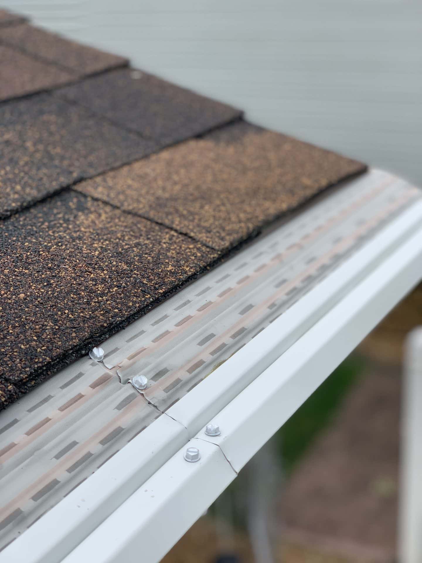 Corner View Of A Shingle Roof And White Gutters With Mesh Gutter Guard Close Up